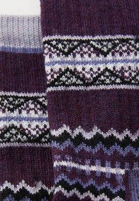 Tejido de punto morado con patrones geométricos en negro, blanco y lavanda. Textura suave con diseños de puntadas variados y acentos en zigzag.