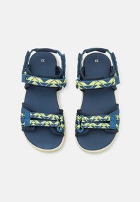 Blå sandaler med mönstrade gröna och gula remmar. Har justerbara spännen och en texturerad sula. Storlek 33 angiven på sulan.