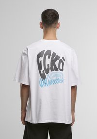 Hvid bomulds T-shirt med stor sort "ECK�Ö" tekst og blå "Unlimited" grafik på ryggen; kortærmet og afslappet pasform.
