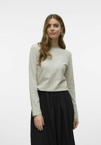 Gestreept longsleeve top in crème met zwarte lijnen, met een boothals en een losse pasvorm. Gecombineerd met een zwarte, geplooide rok.