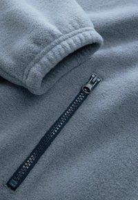 Grijze fleece pullover met een gestructureerd oppervlak, voorzien van een donkere ritssluiting aan de voorkant en een licht elastische manchetten.