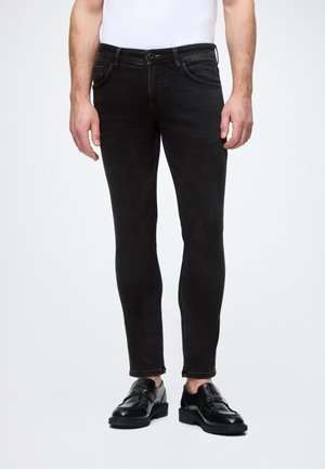 Úzke čierne džínsy s klasickým päť-pocket dizajnom, pútkami na opasok a jemnými prešívacími detailmi, skombinované s čiernymi topánkami.