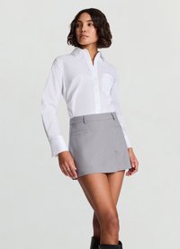 White button-up shirt with a collar and pocket, paired with a light gray tailored mini skirt featuring two front pockets.
