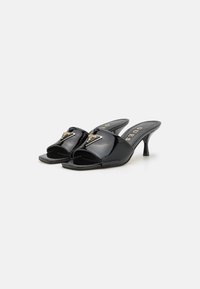 Black patent leather slide sandals feature an open toe, low heel, and a decorative metal logo accent on the upper strap.