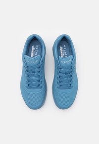 Sapatilhas de desporto azul clara com um cabedal sintético liso, detalhes perfurados, seis orifícios para os atacadores e lingueta e colarinho almofadados.