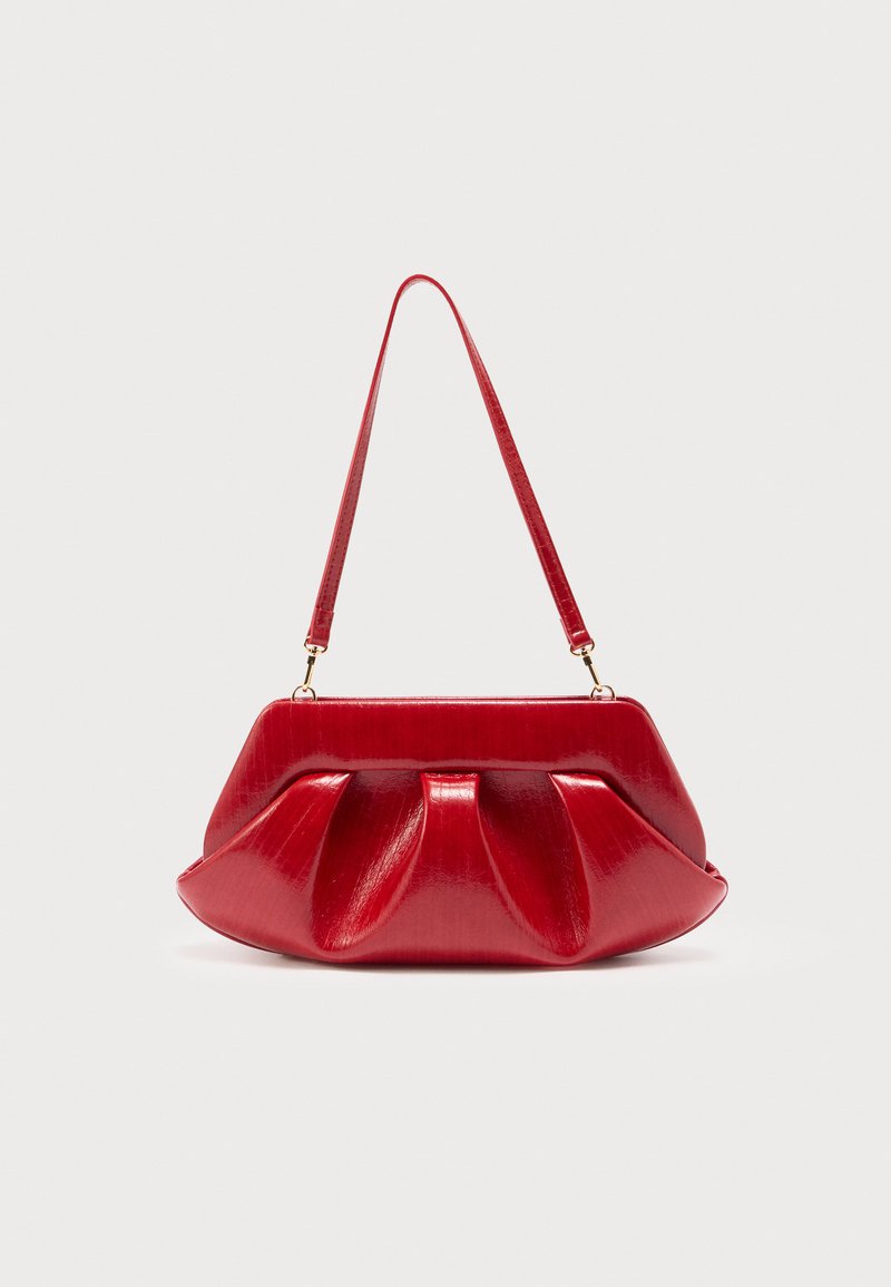 Κόκκινη γυαλιστερή τσάντα χειρός με ρέλι και έναν αποσπώμενο ιμάντα ώμου σε μονόχρωμο φωτεινό φόντο.