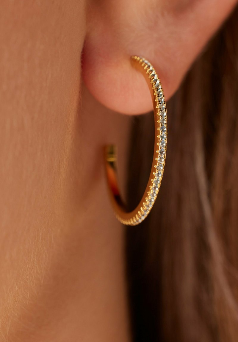 Gouden hoopoorbel met een rij kleine heldere edelstenen langs de voorrand, gladde textuur en een minimalistisch ontwerp.