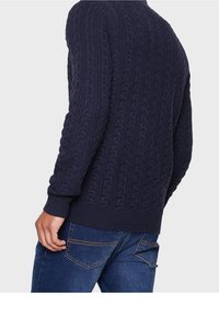 Marineblauer Strickpullover mit strukturiertem Kabelmuster, gerippten Bündchen und Saum. Enganliegendes Design, von der Seite gezeigt, getragen mit blauen Jeans.