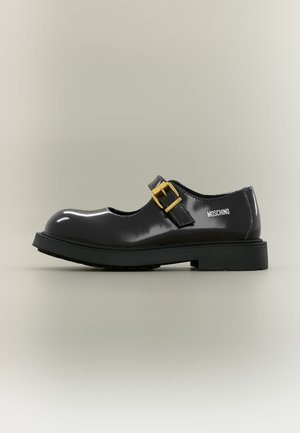 Chaussure Mary Jane en cuir verni noir avec une bride à boucle dorée et une semelle épaisse, avec le logo Moschino sur le côté.