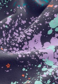 Dark fabric with irregular splatter patterns in purple, light blue, and small orange stars scattered across the surface.