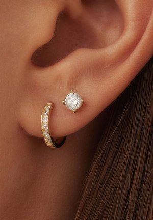 Boucle d'oreille en or avec des pierres claires, accompagnée d'une boucle d'oreille ronde étincelante. Les deux boucles d'oreille sont portées dans la même oreille.
