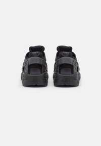 Sapatos desportivos pretos com uma sola de borracha texturizada, suporte acolchoado para o tornozelo e tiras ajustáveis, apresentando "AIR" estampado no calcanhar.