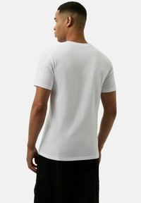 Weißes T-Shirt mit kurzen Ärmeln aus Baumwolle, mit einem klassischen Rundhalsausschnitt. Glatte Textur mit minimalistischem Design, von hinten dargestellt.