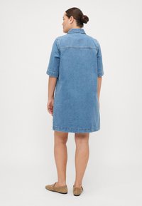 Light blue denim dress with a collar, short sleeves, and a straight silhouette. Back features stitched detailing and a hemline just above the knee.