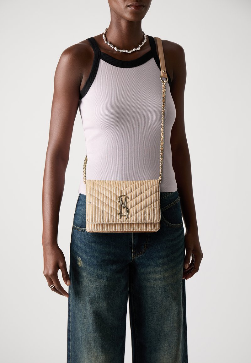 Bolso acolchado beige con una cadena dorada y detalle del logotipo, que muestra una forma rectangular y una superficie texturizada.