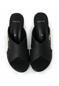 Sandalias negras con tiras cruzadas, hechas de piel texturizada, que cuentan con una planta interna suave. Acabadas con un detalle de hardware dorado en el lateral.