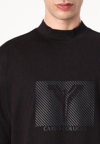 Zwarte katoenen T-shirt met een hoge kraag, voorzien van een textuur zwart grafisch logo en diagonale strepen in het midden.