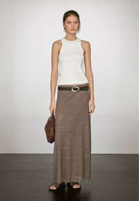 Witte mouwloze top, bruine maxi rok met een riem met een ronde gesp, en een gestructureerde bruine tas. Schoeisel zijn zwarte sandaaltjes met bandjes.