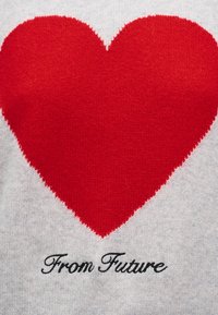 Μεγάλη κόκκινη καρδιά πλεγμένη πάνω σε γκρι ύφασμα με μαύρο διακοσμητικό κείμενο «Από το Μέλλον» κάτω από την καρδιά.