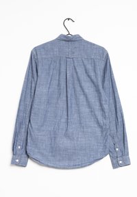 Pitkähihaista sinistä chambray-paitaa, jossa on kaareva helma, kaulus ja napilliset hihansuut. Kangas on tekstuuriltaan kudottu ja siinä on hienovaraisia vaaleita kuvioita.