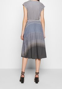 Blå och vit mönstrad klänning med korta ärmar, plisserad kjol och en gradient från blått till svart vid fållen. Stylandes med svarta klackskor med blockklack.