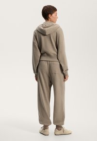 Hoodie grigio chiaro in tessuto morbido con vestibilità rilassata, dotato di tasca a marsupio e polsini a costine, abbinato a pantaloni larghi coordinati.