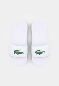 Sandales blanches à glissière avec une large bride arborant un logo de crocodile vert, en matériau lisse et au design minimaliste.