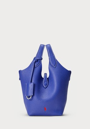 Zila ādas soma ar akmens tekstūru, kurai ir divas augšējās rokas, izgriezuma dizains un sarkans logotipa akcentu priekšpusē.