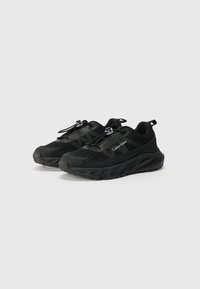 Baskets noires avec un dessus texturé, présentant un design en maille et des lacets élastiques, reposant sur une semelle épaisse et nervurée. Logo Calvin Klein visible.