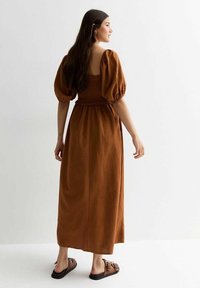 Bruine maxi-jurk met pofmouwen, gerimpelde buste en een vierkante rug. Draag met zwarte instap-sandalen. Smooth, lichtgewicht materiaal.