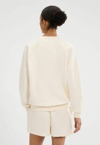 Licht beige sweatshirt met een relaxed fit en verlaagde schouders, gemaakt van zachte katoen. Heeft ribgebreide boorden en een eenvoudig ontwerp.