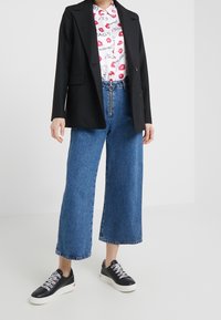 Svart skräddarsydd blazer, vit skjorta med röd läpptryck, vida blå denimjeans och svarta sneakers med vita sula och färgade snörningar.