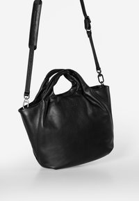 Zwarte leren handtas met een zachte, textuurafwerking. Voorzien van dubbele handvatten en een verstelbare schouderband. Compacte, afgeronde vorm.