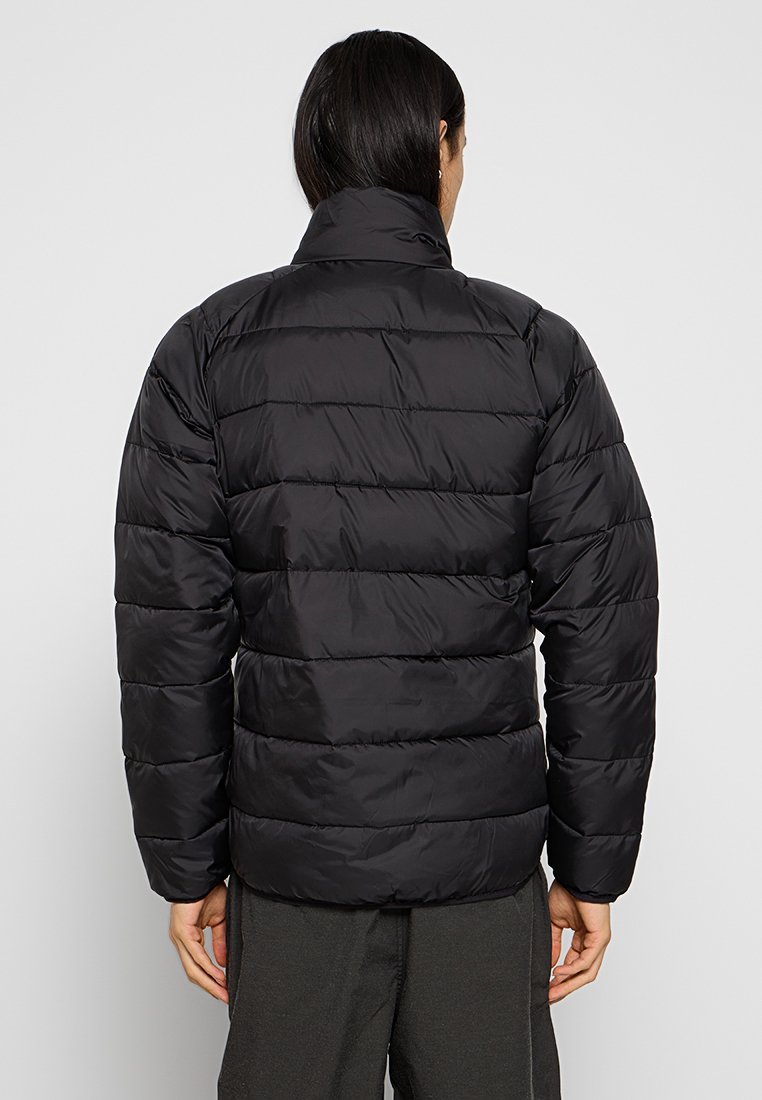 Giacca a vento nera con texture trapuntata orizzontale, colletto alto e polsini elasticizzati. Materiale leggero e idrorepellente con tasche nascoste.