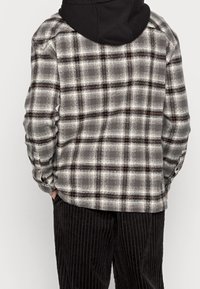 Grijze en zwarte geruite blouse met rode accenten, lange mouwen, knopenmanchetten en een relaxte pasvorm, gecombineerd met zwarte corduroy broek.