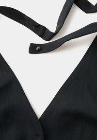 Vêtement en tissu noir avec encolure en V et une sangle noire attachée présentant un petit bouton noir et des boutonnières sur fond blanc.
