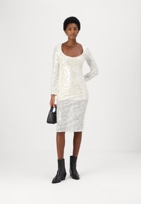 Puku sequined yenye mikono mirefu, shingo ya kuingia, umbo lililofanywa kuwa na mtego, likibadilika kutoka rangi ya cream hadi silver, likifanyika na viatu vya ankle vya rangi ya black na mkono mdogo wa kubebea.