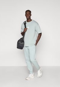 Ανοιχτό πράσινο υπερμεγέθες μπλουζάκι και τζόκεϊ παντελόνια με στενή γραμμή. Μαύρη τσάντα ώμου. Λευκά αθλητικά παπούτσια με γκρι λεπτομέρειες. Απλός σχεδιασμός.