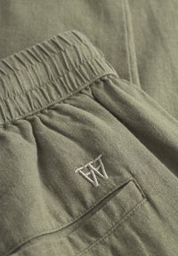 Grüne Baumwollhose mit elastischem Bund, gesticktem Logo in Weiß und strukturiertem Stoff im lässigen Schnitt.
