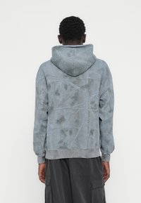 Φούτερ με κουκούλα σε ήσυχο μπλε χρώμα με υφασμένο σχέδιο κλαδιών δέντρου. Διαθέτει ριμπ μανσέτες και τελείωμα, καθώς και τσέπη καγκουρό.