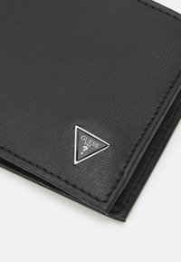 Portefeuille en cuir noir avec une surface texturée, un accent en logo argenté en forme de triangle et une couture contrastante sur les bords.