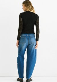 Black long-sleeve top with textured knit pattern, paired with high-waisted, faded blue denim jeans. Smooth fabric and relaxed fit.