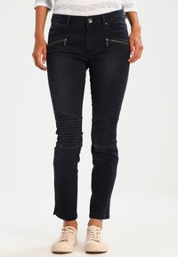 Tmavě modré džíny s ribovanými akcenty na kolenou, zipovými předními kapsami a slim fit střihem. Materiál je denim, s hladkým povrchem a mírnou elasticitou.