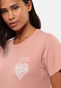 Lichtroze T-shirt met korte mouwen featuring een witte grafische hartontwerp met bloemen- en vlinderpatronen, gemaakt van een zachte, rekbare stof.