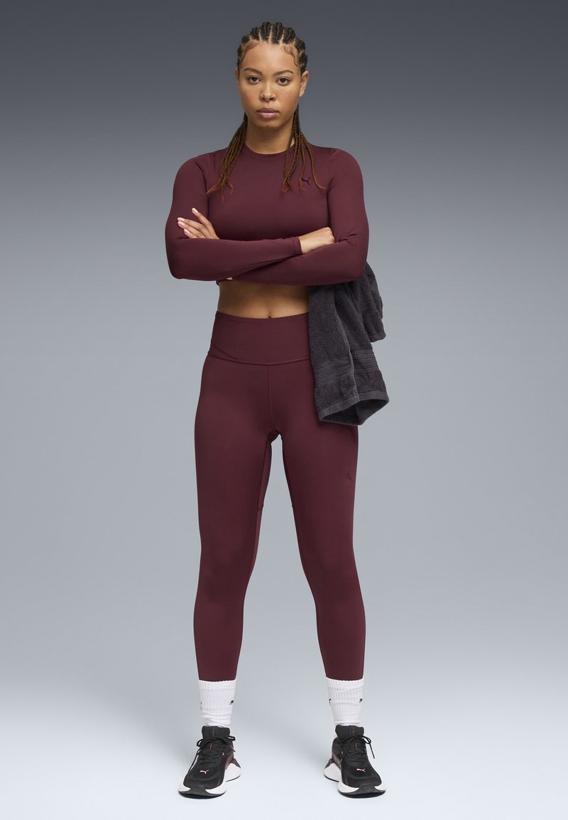 Maroon long-sleeve athletic top and matching high-waisted leggings, with a textured dark towel draped over one arm and black athletic shoes.
