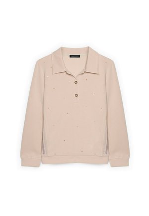 Beige langærmet polo med krave, to knapper, små sølv- og guldfarvede nitter spredt på fronten og netpaneler i siden.