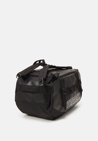 Sac de sport noir en tissu durable et texturé, avec des sangles réglables et plusieurs poignées latérales. Comprend le logo "TERREX" en blanc.