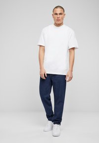 Camiseta de algodón blanca con un corte holgado, combinada con jeans de mezclilla azul marino. Calzado: zapatillas blancas. Diseño simple sin patrones visibles.