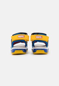 Zili un dzelteni sandales ar regulējamiem siksniņām, kurām ir sarkans "MARVEL" logotips. Šiem apaviem ir acs iekšpuse un gumijas zole.