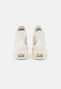 Beżowe wysokie trampki Converse All Star z kwiatowymi naszywkami i tekstem "JESTEŚMY SILNIEJSI RAZEM" wewnątrz pięt.